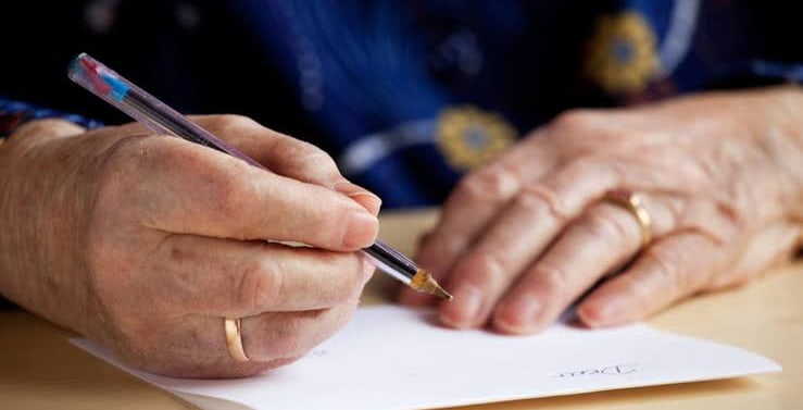 Manos de una persona mayor escribiendo una carta